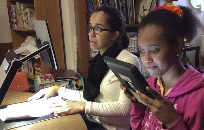 Two female students one using a book magnifier and the other using her iPad