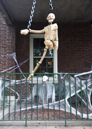 Chained manequin skeleton hangs suspended over porch rail. 